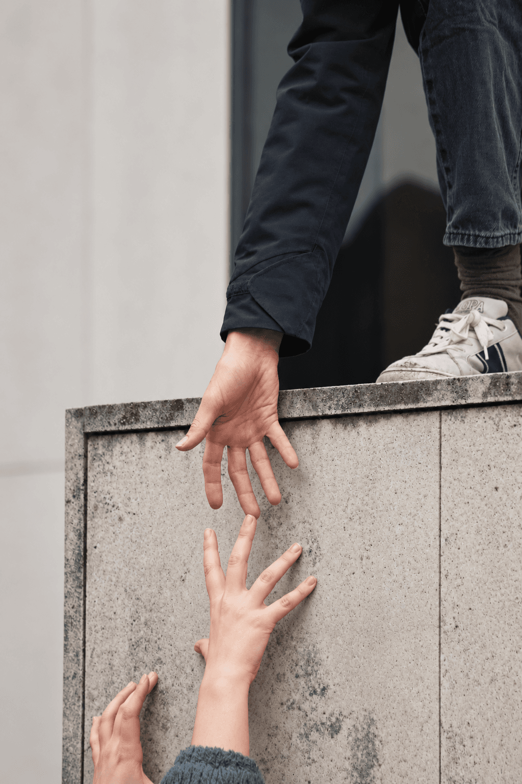 A person reaching down to help others over a wall